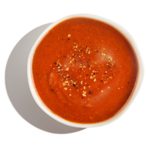 A bowl of tomato soup on a white surface.