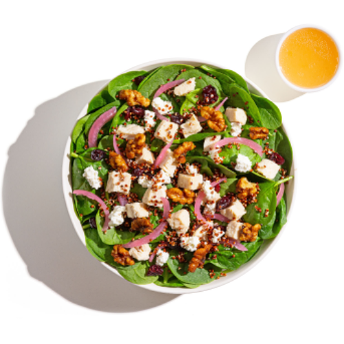 A healthy salad with fresh spinach leaves, crumbled feta cheese, and crunchy walnuts. At the side of the bowl, a glass of orange juice.