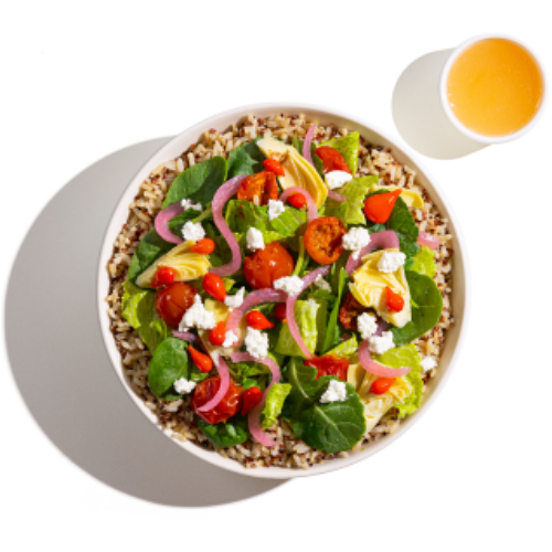 A bowl filled with grains, toped with vibrant vegetables, tomatoes and grated cheese. On the side, a glass with an orage juice.